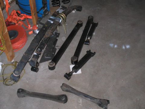 1991 Ford Bronco - Collection of suspension components, including leaf springs and control arms, laid out on a garage floor.