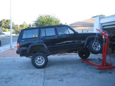 1991 Ford Bronco - A black Jeep Cherokee XJ is being worked on with a red engine hoist lifting the front wheel.