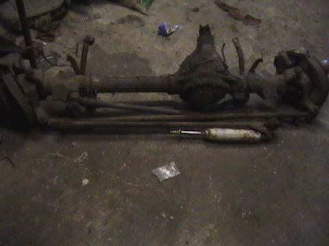 1986 Ford Bronco - A disassembled front axle assembly and a shock absorber lie on a concrete floor.