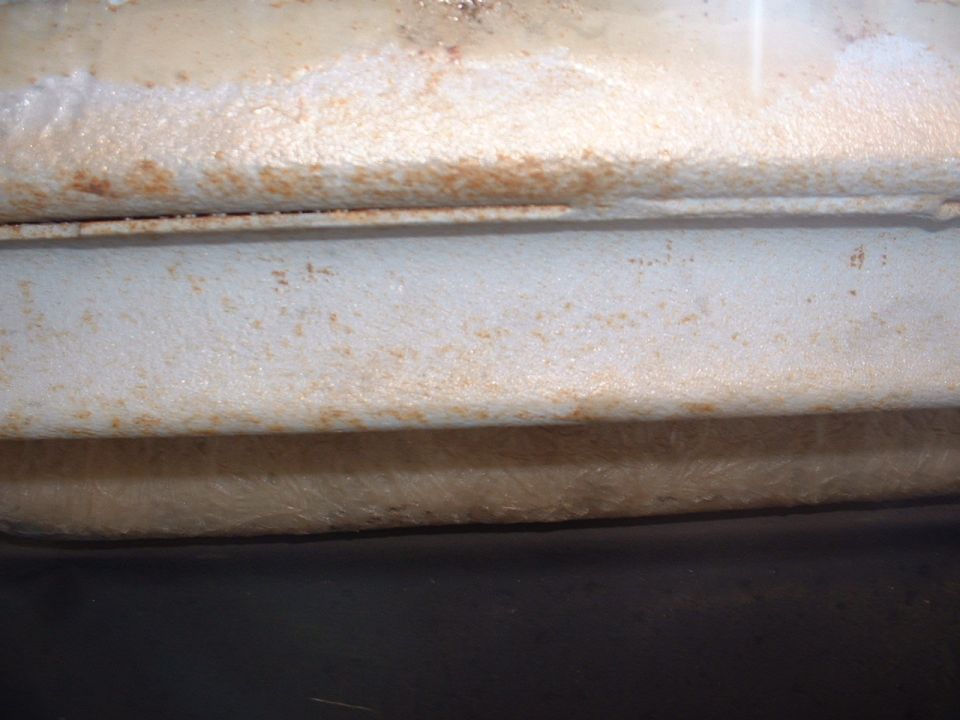 Close-up of a rusted, white painted metal frame section with visible texture and some dirt