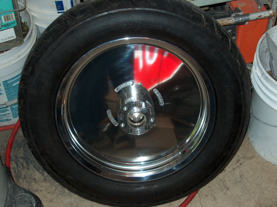 Chrome motorcycle wheel with tire, showing reflection of red and white sign