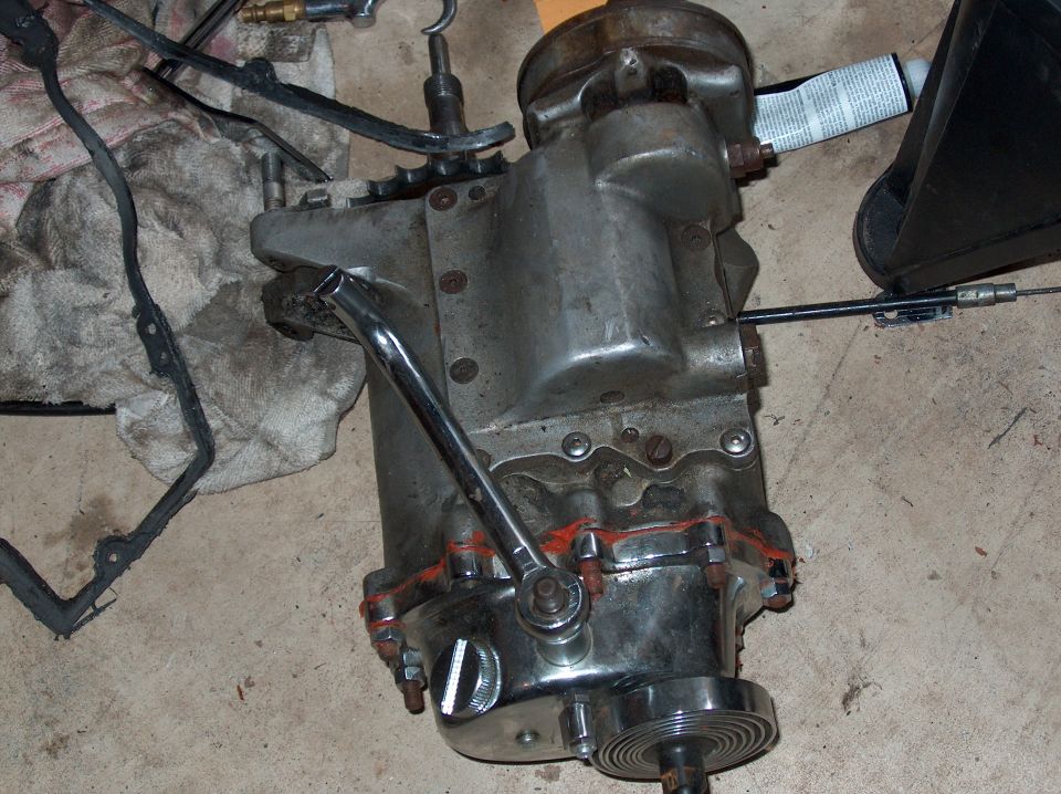 motorcycle transmission with shift lever and cable attached, on a concrete floor with rags