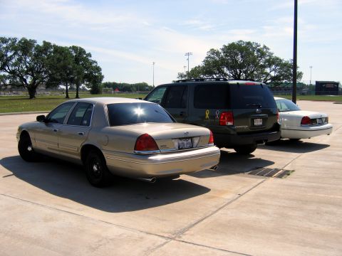 2000 Ford Crown Victoria - Three vehicles are parked in a lot, including a gold 2000 Ford Crown Victoria sedan in the foreground.