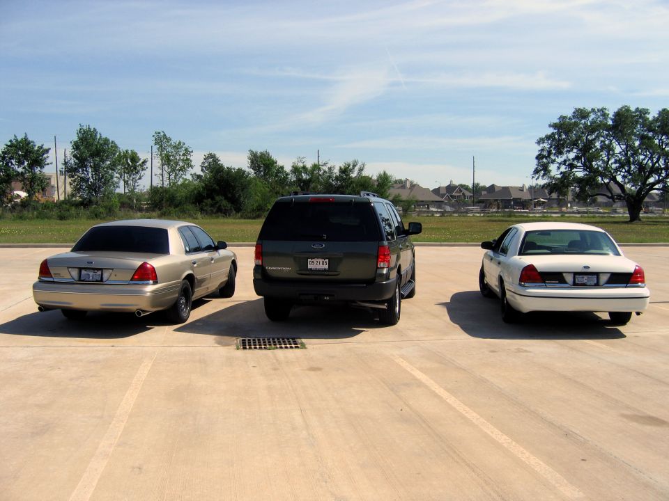 Two 2000 Ford Crown Victorias and a dark SUV parked in a lot