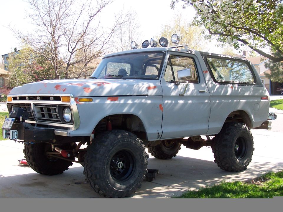 Primer-gray lifted full-size Ford Bronco with roof lights and winch bumper in a driveway