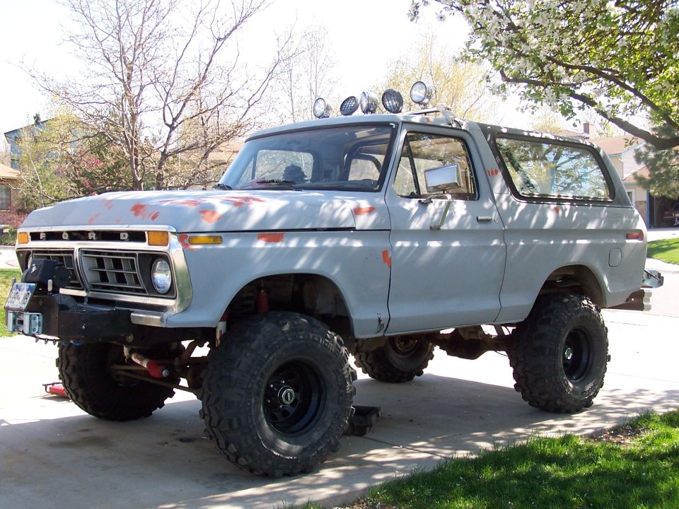 Gray 1978-79 Ford Bronco lifted on mud tires with roof light bar in a driveway