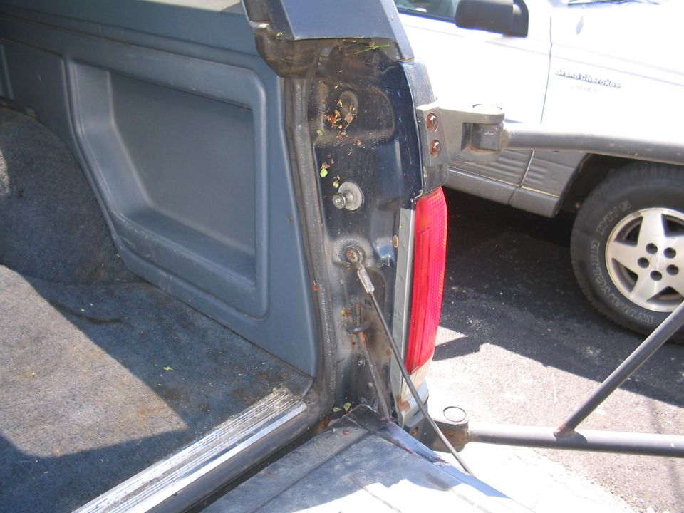 Dark blue SUV interior with gray plastic paneling and worn carpet. A silver SUV is parked behind it