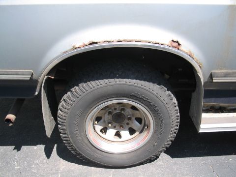 1979 Ford Bronco - Close-up of a rusty wheel well and tire, showing significant corrosion around the fender opening.