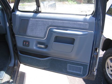1979 Ford Bronco - Close-up of the blue interior door panel, showing the fabric insert, speaker grille, and power window controls.