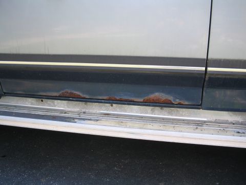 1979 Ford Bronco - The lower body panel of a vehicle shows significant rust damage along the trim line.