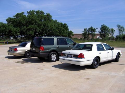 2000 Ford Crown Victoria - Three vehicles are parked in a lot under a blue sky with trees in the background.
