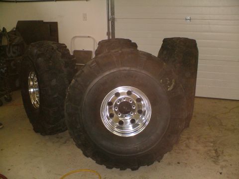 1995 Ford F-150 - A collection of four large off-road tires, each fitted with a shiny chrome rim, are displayed indoors.