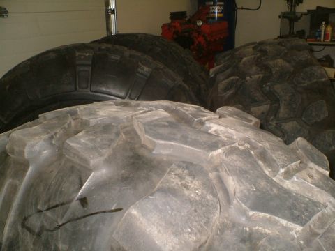 1995 Ford F-150 - Several large tires are visible in a garage setting, with a red piece of machinery behind them.