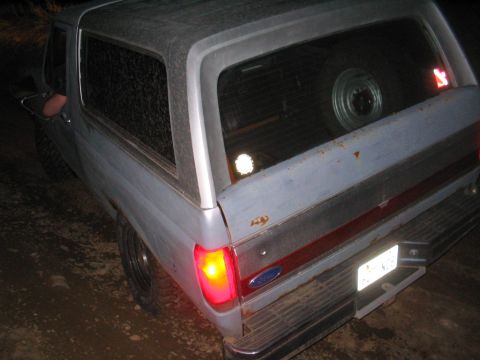 1991 Ford Bronco - The rear of a gray 1987 Ford Bronco is visible, with a spare tire mounted inside and a red stripe accent on the tailgate.