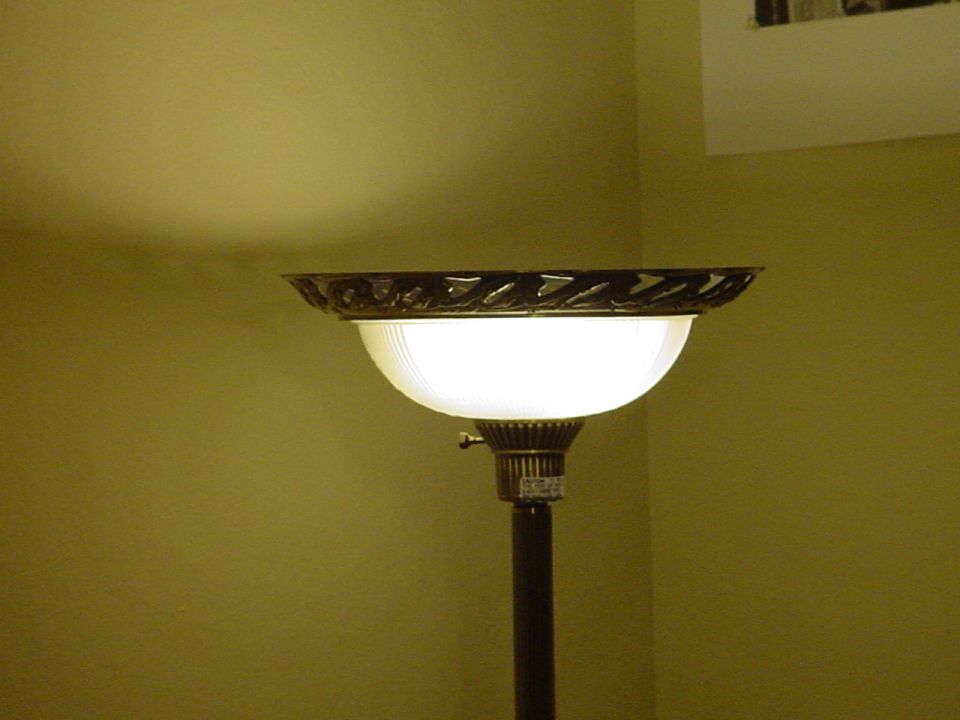 Lit torchiere floor lamp with frosted glass shade in a room corner