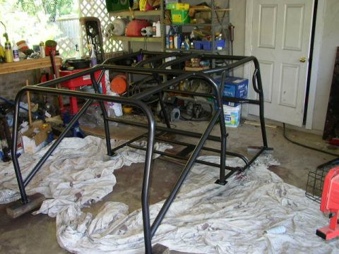 1995 Ford Bronco - A black metal roll cage frame sits on drop cloths in a cluttered garage.