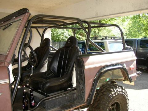 1995 Ford Bronco - This modified Ford Bronco features a custom roll cage and racing seats, with other vehicles visible in the background.