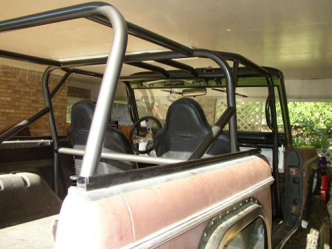 1995 Ford Bronco - The interior of a vehicle is visible, a prominent roll cage, black bucket seats, and a custom steering wheel.