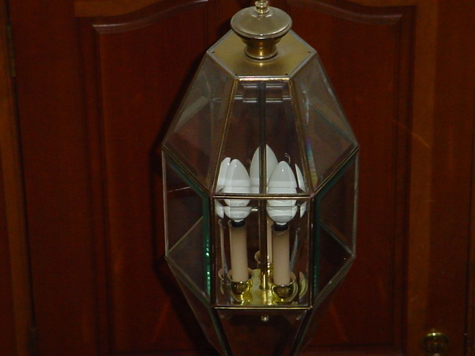 Glass and brass lantern with four light bulbs, hanging against a wooden background