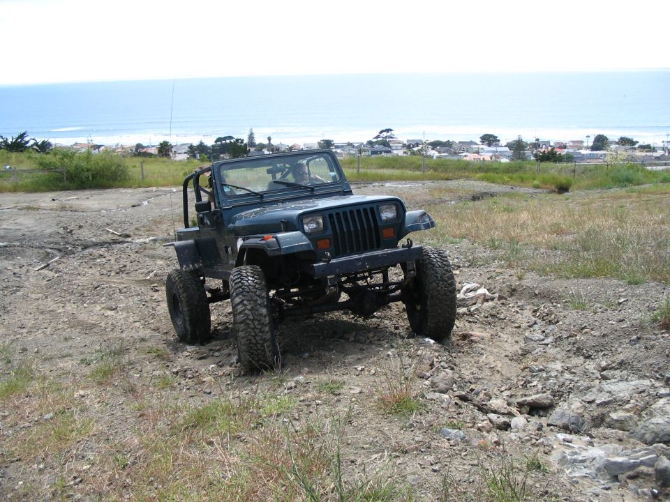 Lifted Jeep Wrangler YJ on muddy tires parked on a coastal hill above ocean