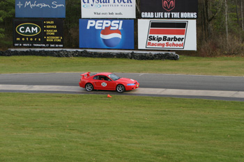 2000 Ford Mustang - A red 2000 Ford Mustang races on a track with advertising billboards in the background.