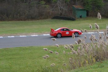 2000 Ford Mustang - A red sports car with a prominent spoiler navigates a grassy track, displaying the number 02.
