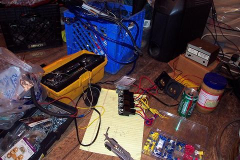 1985 Ford LTD Crown Victoria - Various automotive electrical parts and wiring are spread out on a wooden floor, suggesting a repair or installation project.