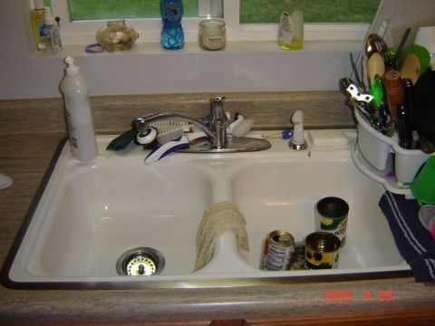 1993 Ford Bronco - A double kitchen sink holds dish soap, cleaning brushes, and several cans of food, with a dish rack full of utensils to the right.