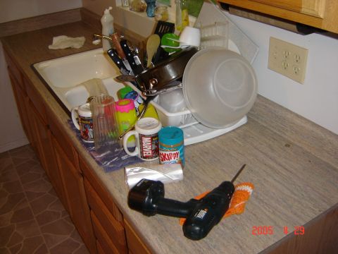 1993 Ford Bronco - A drill sits on a counter next to a sink filled with dirty dishes and various kitchen items.