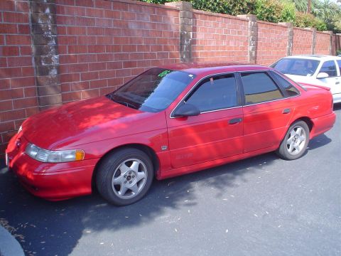1993 Ford Taurus - Side view of a red 1993 Ford Taurus parked outdoors. A white car is parked behind it.