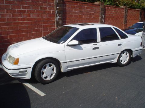 1993 Ford Taurus - A white sedan with tinted windows and a sunroof is parked in a lot.