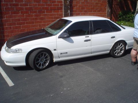 1993 Ford Taurus - This sedan, likely a mid-1990s model, has a black hood and aftermarket wheels.