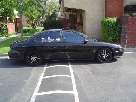 1993 Ford Taurus - A black sedan with custom rims and stickers on the window is parked in a lot.