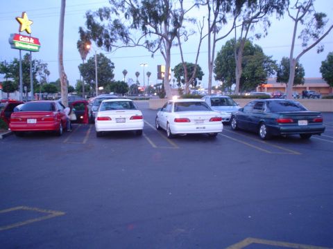 1993 Ford Taurus - Several cars are parked in a lot near a Carls Jr. restaurant at dusk.