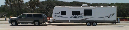 2004 Ford Excursion - A Ford Excursion tows a large travel trailer down a road with trees in the background.