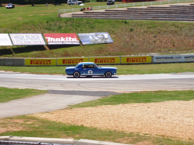Blue Mustang race car #2 in side view on a race track with Pirelli sponsor banners behind