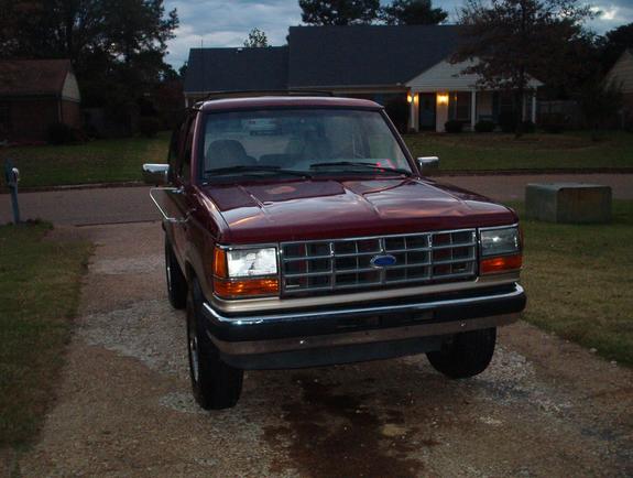 Front view of a dark red Ford Bronco II with tan lower trim and chrome grille on a gravel driveway at dusk