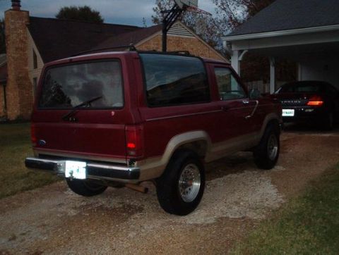 1989 Ford Bronco II - A red 1989 Ford Bronco II is parked outside a house with a second vehicle in the garage.