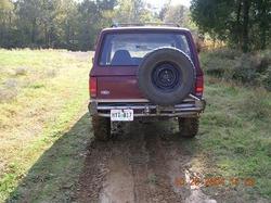 1989 Ford Bronco II - Rear view of a maroon 1989 Ford Bronco II with a spare tire mounted on the rear bumper, parked on a dirt road.