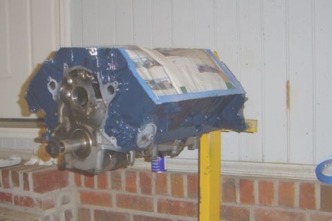 1986 Ford Bronco - Engine block is partially covered with newspaper and blue tape, resting on a yellow stand.
