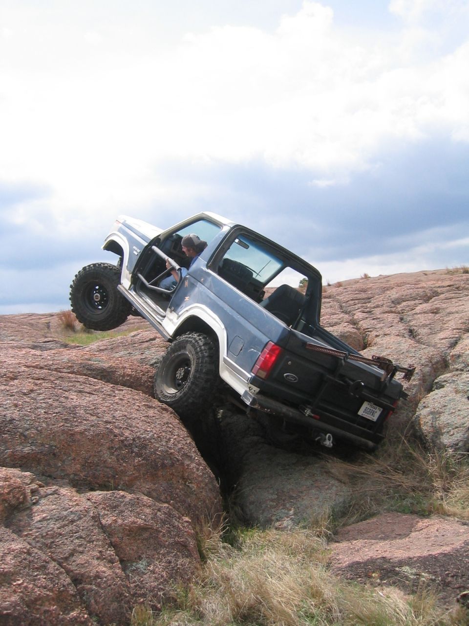 Blue and white off-road SUV climbing rocks, 1980s body style