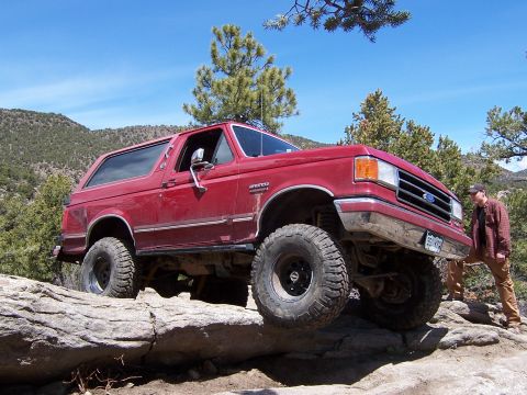 1991 Ford Bronco - Red 1991 Ford Bronco navigating a challenging rocky terrain during an off-road excursion.