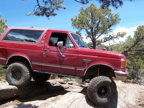 1991 Ford Bronco - This red Ford Bronco is navigating a rocky off-road course under a clear blue sky.
