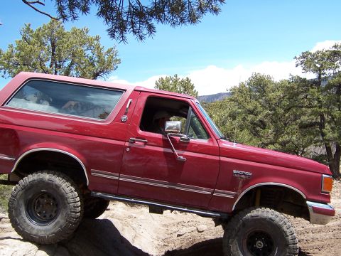 1991 Ford Bronco - A red 1992 Ford Bronco navigates a rocky, off-road trail under a clear blue sky.