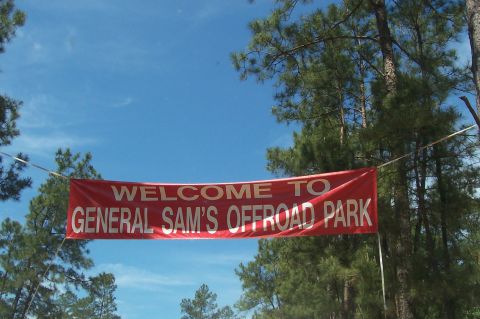 1989 Ford Bronco - Welcome banner for General Sam's Offroad Park hangs under a blue sky with trees.