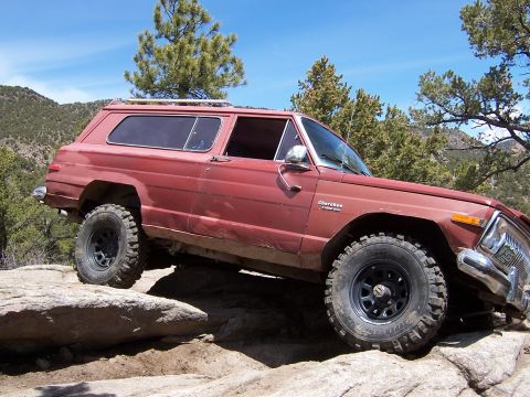 1991 Ford Bronco - This Jeep Cherokee Chief is navigating a rocky trail under a clear blue sky.