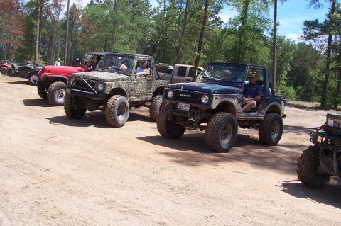1989 Ford Bronco - Multiple Suzuki Samurai vehicles are lined up on a dirt trail in a wooded area.