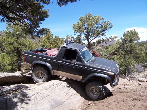 1991 Ford Bronco - A modified Ford Bronco navigates a rocky trail under a clear blue sky.
