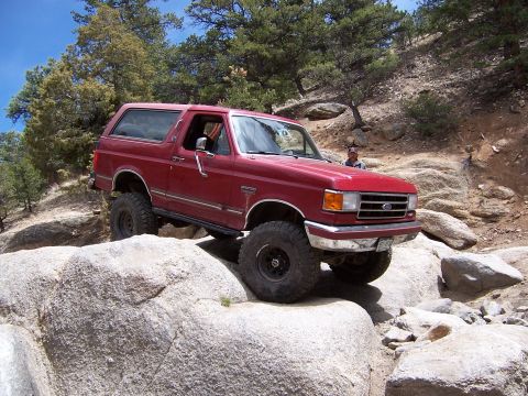1991 Ford Bronco - Red 1991 Ford Bronco climbs over large rocks on a trail.