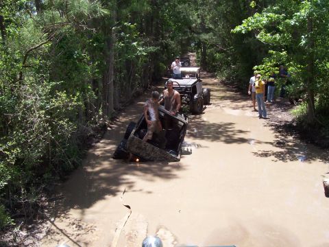 1989 Ford Bronco - Multiple off-road vehicles navigate a muddy trail, with some appearing stuck.